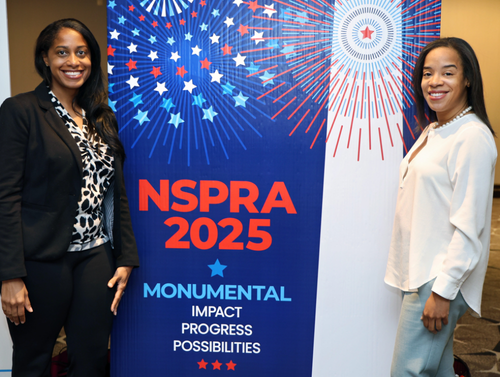 Two NSPRA 2025 National Seminar attendees pose in front of the Monumental Impact event backdrop.